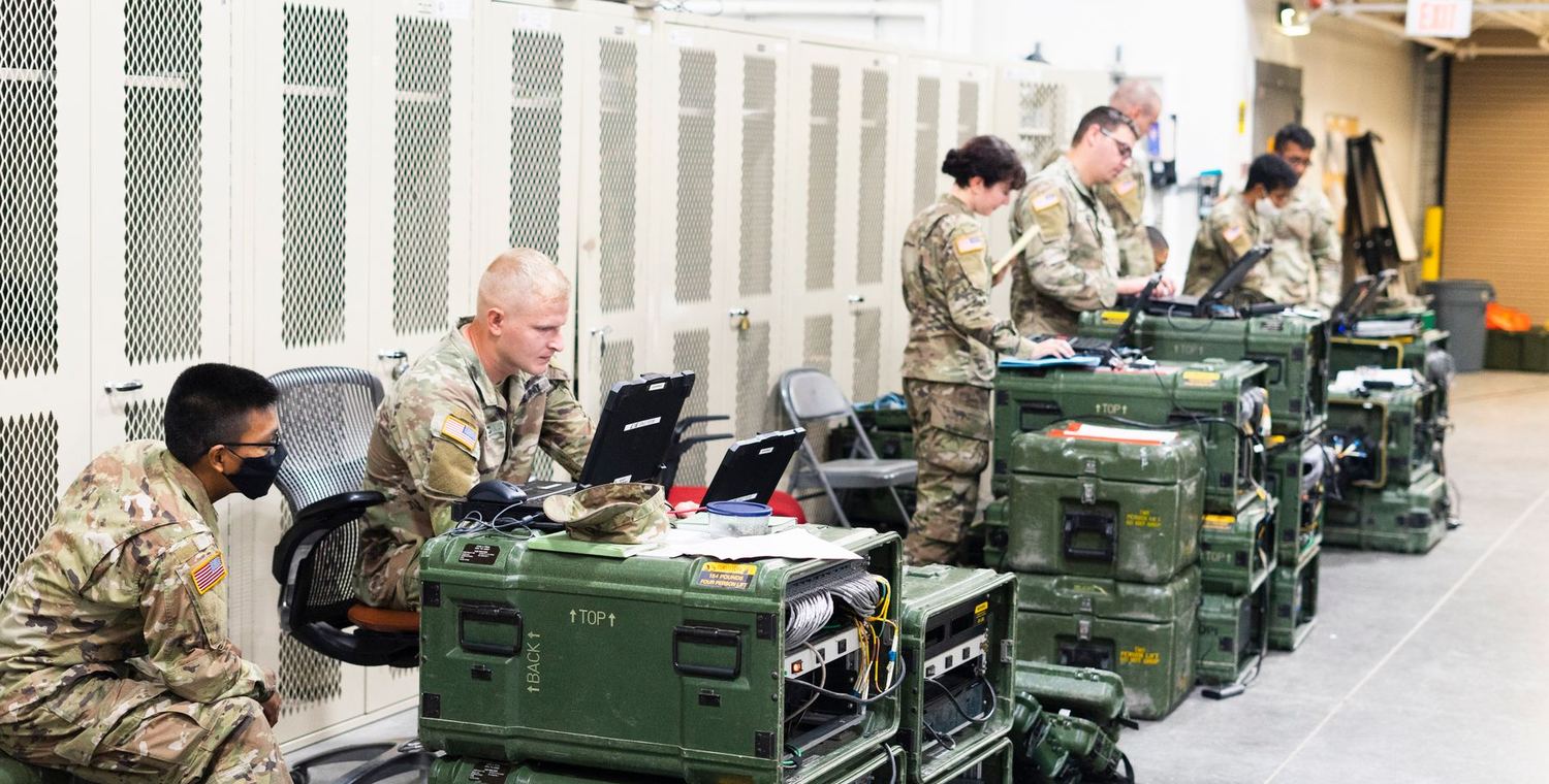 Military personnel working at ruggedised laptops on deployable equipment cases in a field operations centre